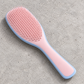 Pink blue Knotty Brush detangling hair brush with pink bristles and a blue edge on a concrete surface