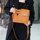 Model wearing a brown structured crossbody bag with lock buckle, strap worn across the body