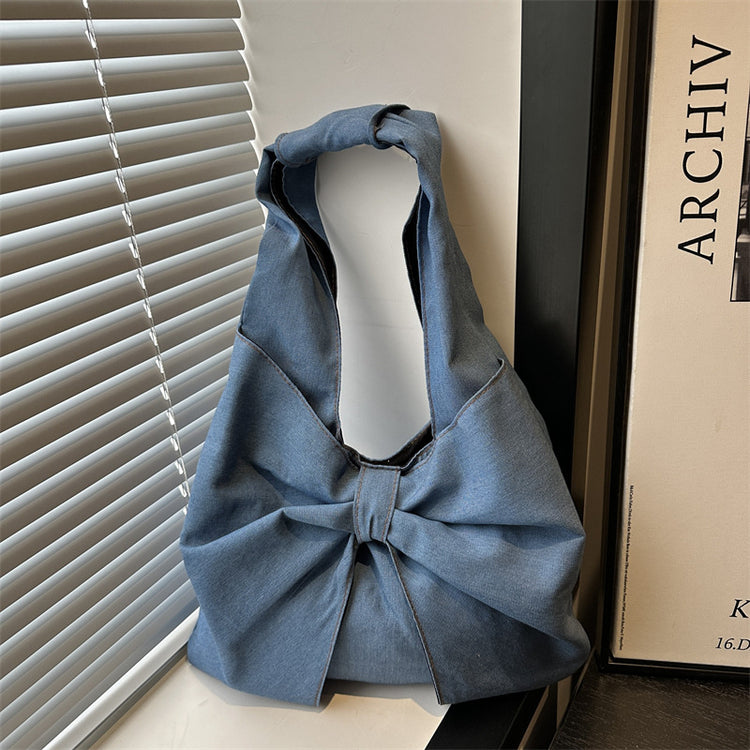 Blue denim bow shoulder bag with oversized bow in front of window blinds