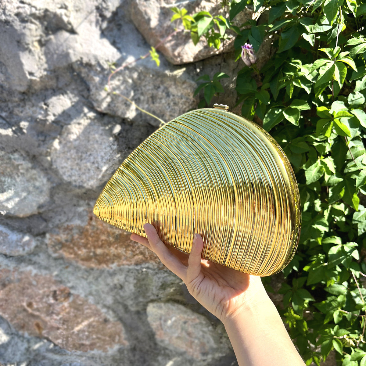 Hand holding a yellow glass lamp against a stone wall and green foliage background
