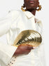 A model holding a gold clutch with a white outfit and gold earrings.